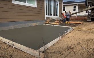 Crew pouring concrete for steps next to a concrete slab.
